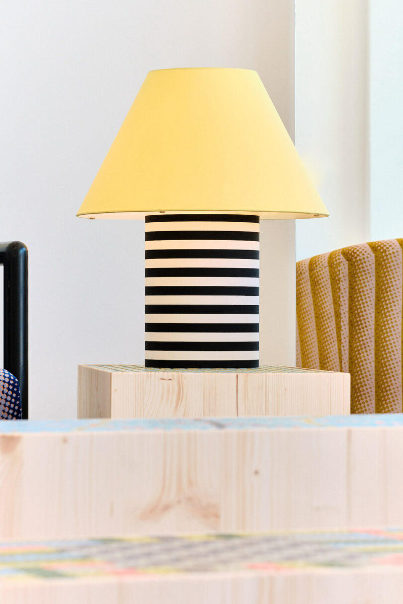 A lamp with a yellow shade and black-and-white striped base on a light wooden table