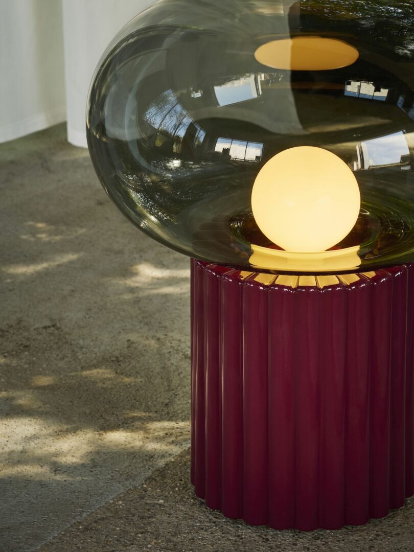 Modern lamp with a round light bulb encased in a glass orb, resting on a ribbed, maroon base