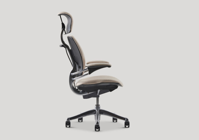 Side view of an ergonomic office chair with a beige seat and backrest, featuring adjustable headrest and armrests, on a five-wheel base