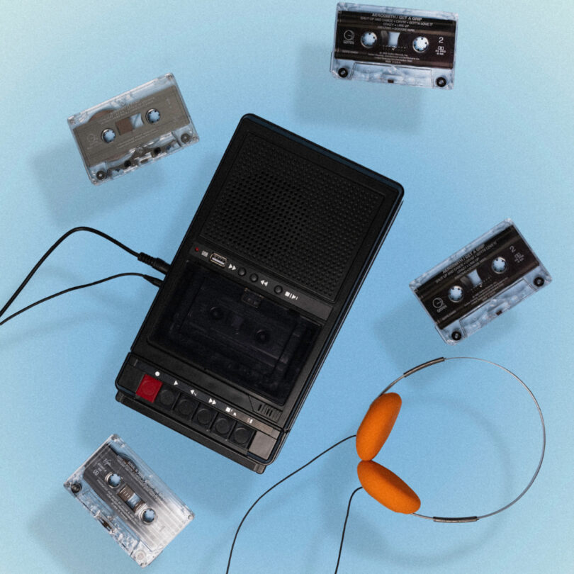 A black portable cassette player with headphones and five cassette tapes on a light blue background.