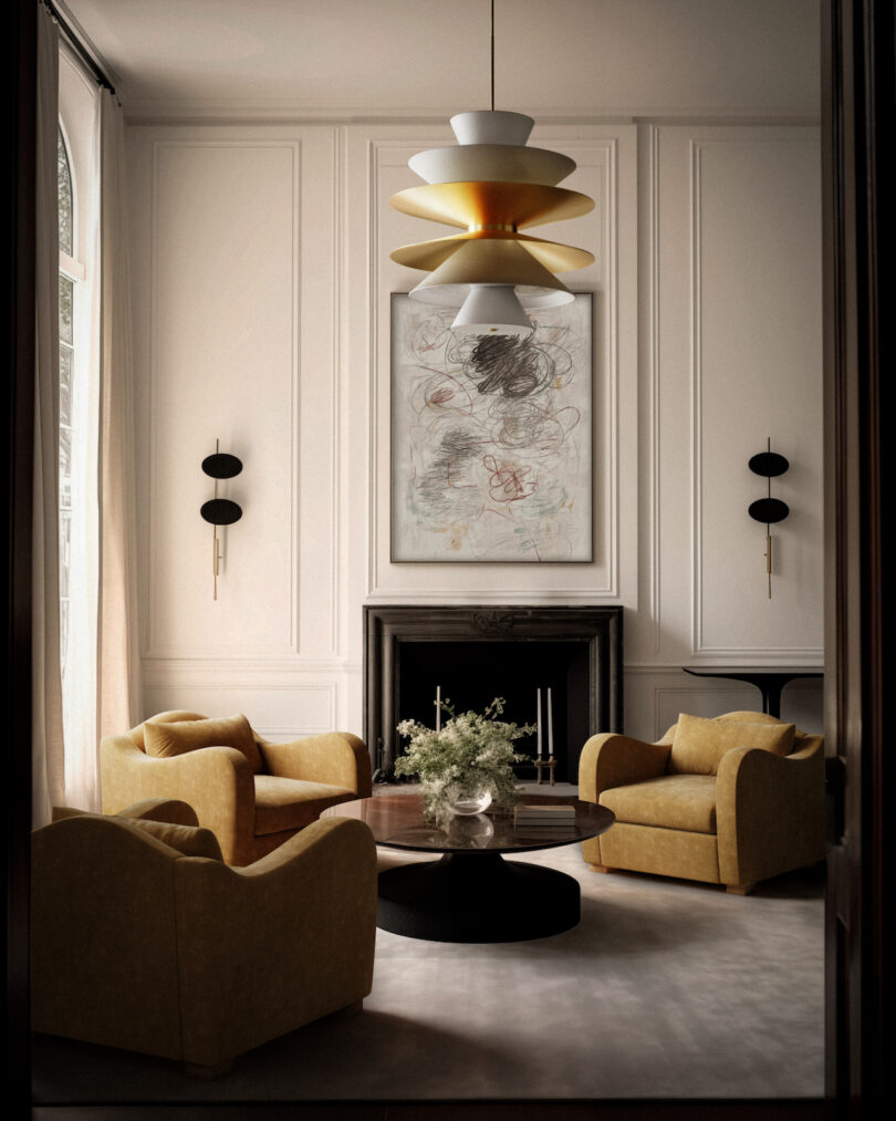 A cozy living room with four yellow armchairs around a dark circular coffee table, beneath a modern chandelier, and abstract art above a fireplace