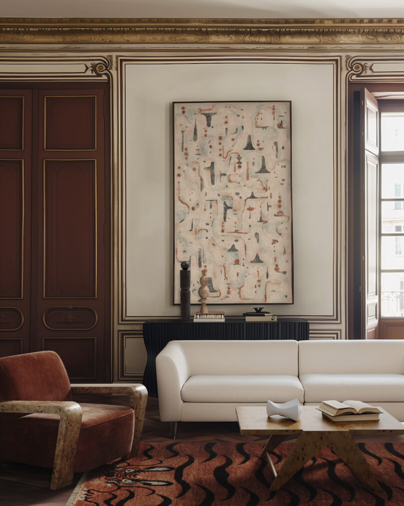 A living room with a white sofa, brown armchair, abstract artwork on the wall, and a wooden coffee table on a patterned rug