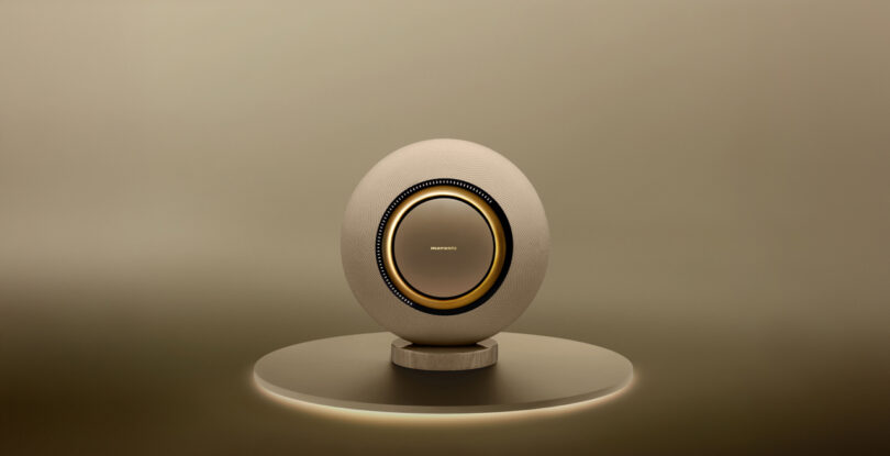 A spherical speaker with a central circular design, displayed on a round platform against a beige background.