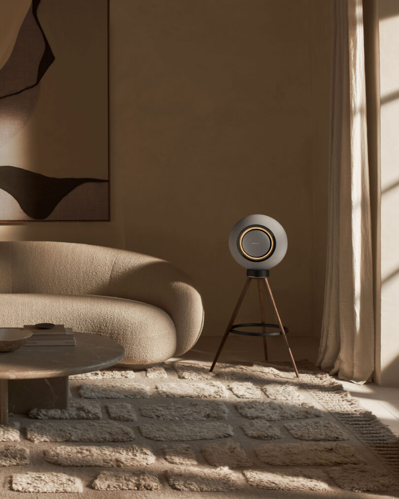 Minimalist living room with a curved sofa, a tripod speaker, a low table, and a textured rug in warm lighting.