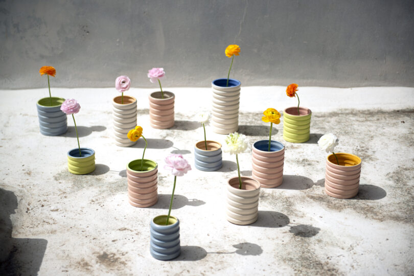 Colorful ceramic vases with single flowers arranged on a sunlit concrete surface