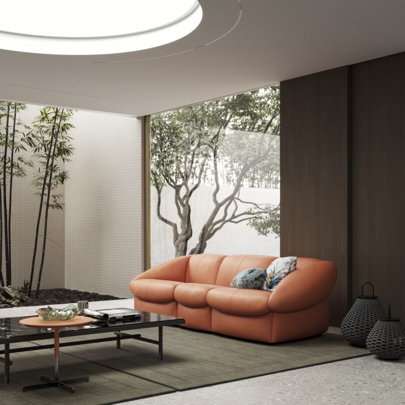 Cozy living area with an orange sofa, pillows, black table, and decorative items. Large window view of bamboo plants and a tree in a minimalist setting