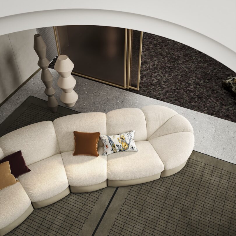 Top view of a modern living room with a curved beige sofa, patterned pillows, a geometric lamp, and a checkered rug on a speckled and textured floor.