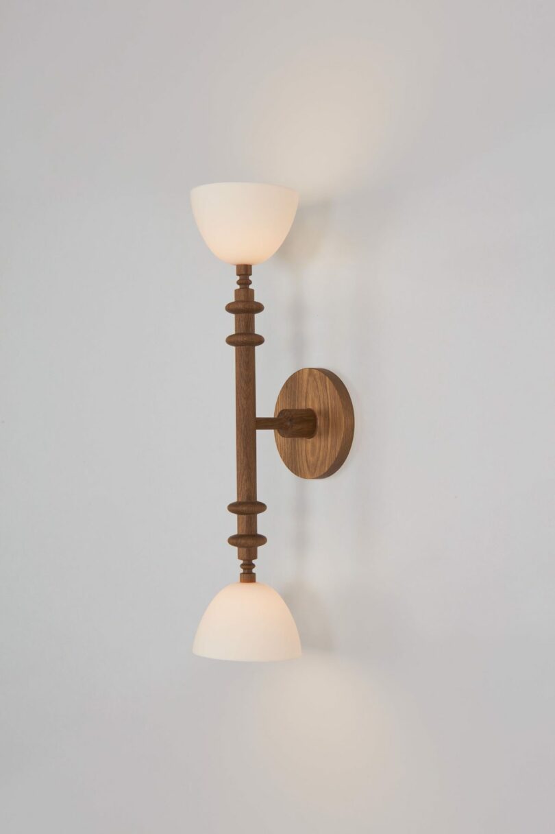 A wooden double-sconce wall light with white glass shades mounted on a white wall