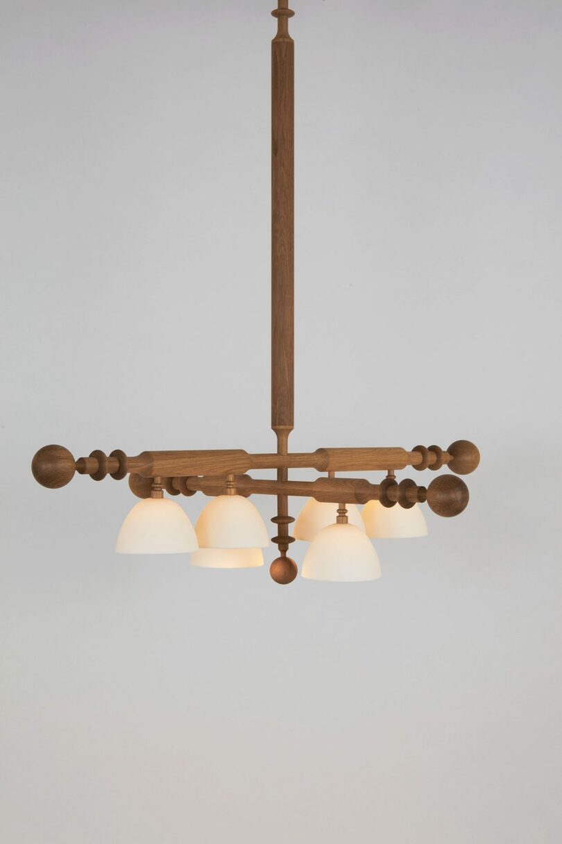 A wooden chandelier with five white lampshades, suspended from a ceiling