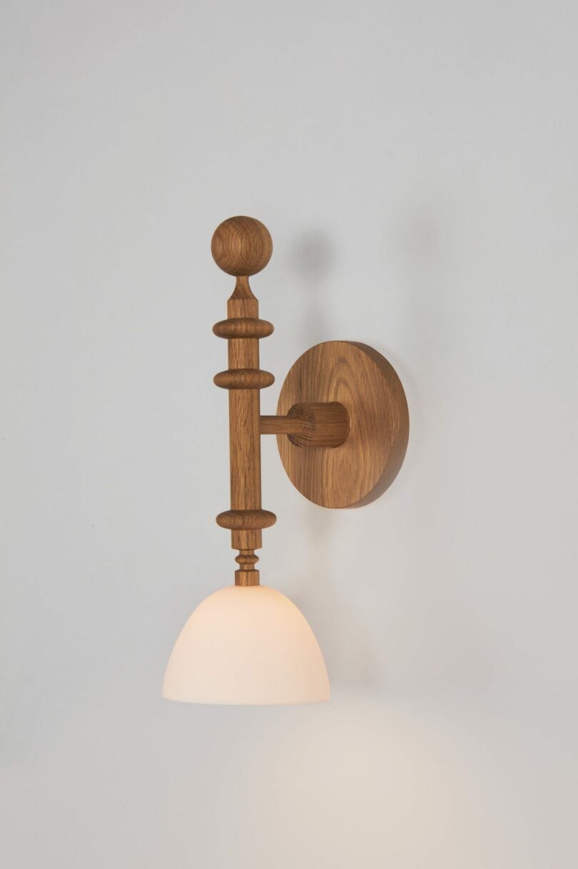 A wooden wall-mounted lamp with a round base and a downward-facing white lampshade