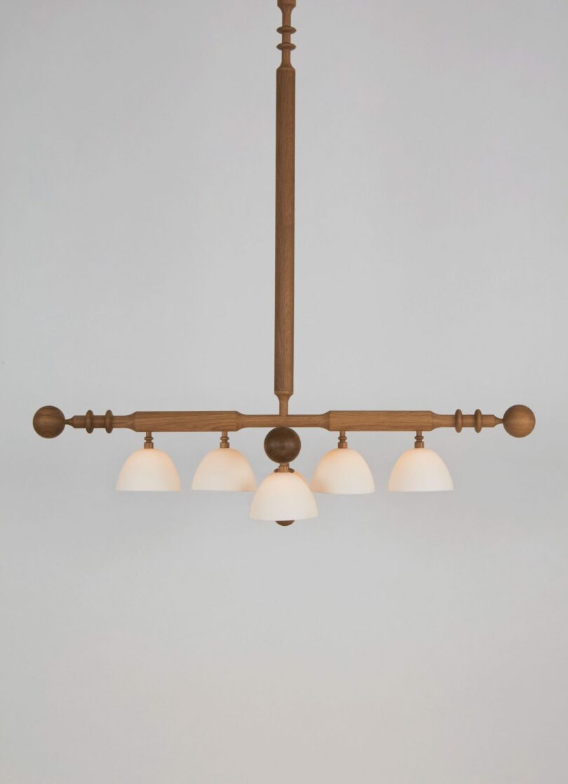 A wooden light fixture with five white dome-shaped lampshades suspended from a central rod