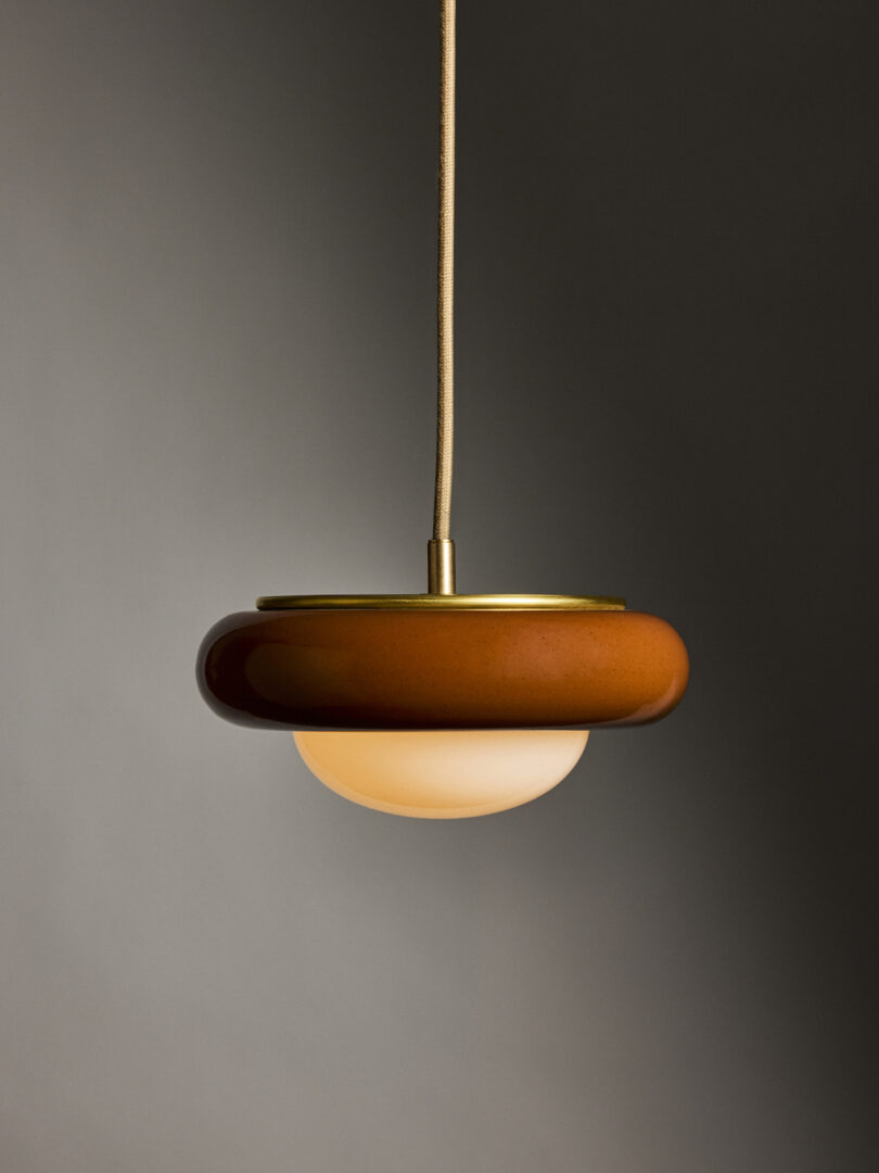 A pendant light with a round, brown outer ring and a white inner globe hanging from a beige cord against a gray background