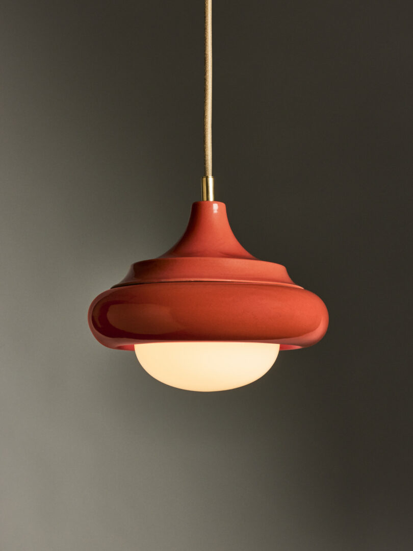 Red hanging lamp with a round, smooth design, featuring a white diffuser, against a plain gray background