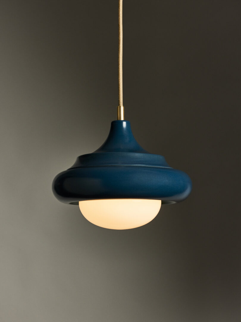 A blue pendant light with a rounded shape and a white diffuser is suspended from the ceiling against a gray background