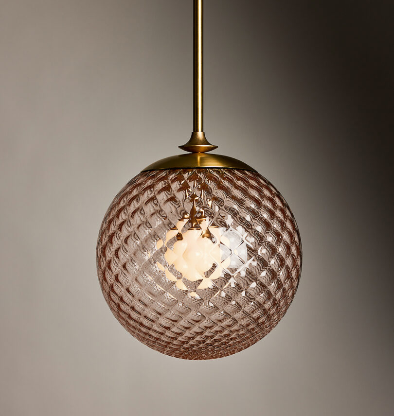 Round glass pendant light with a textured pattern and brass fixture, hanging against a plain background