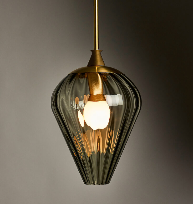 A pendant light with a brass fixture and a ribbed glass shade, illuminated against a plain background