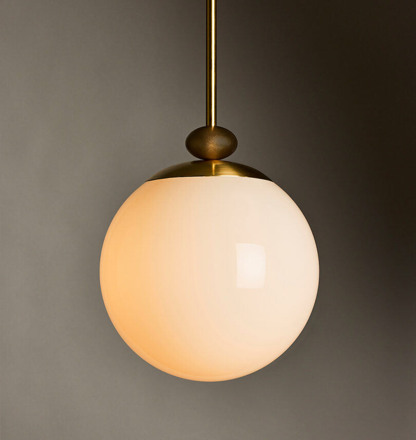 A spherical pendant light with a matte brass fixture, suspended from the ceiling against a gray background