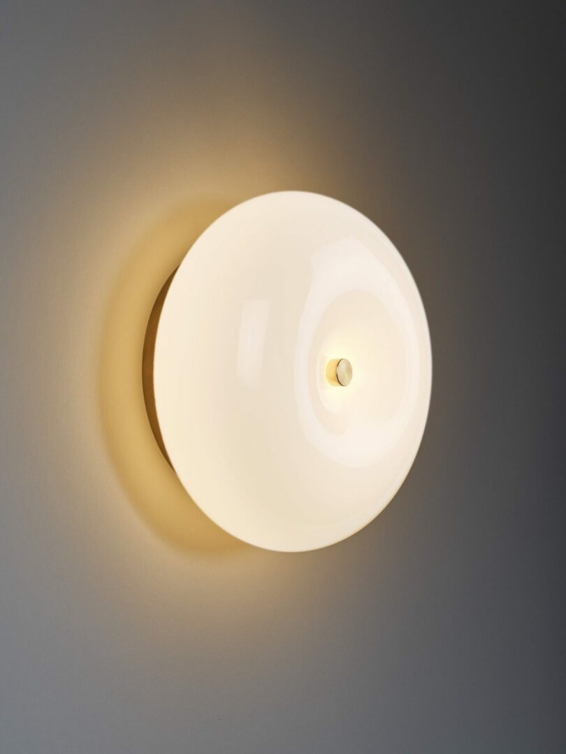 A round, wall-mounted sconce with a white, glowing bulb against a light-colored wall