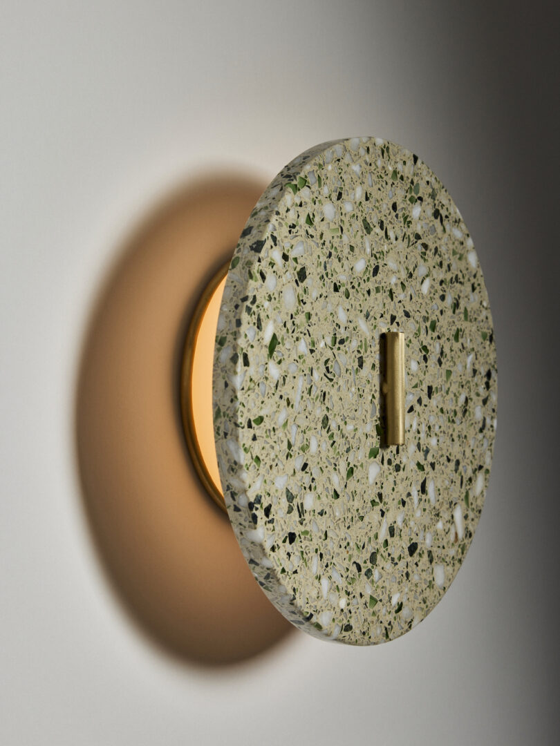 A round, terrazzo-patterned wall sconce with a warm light glows against a white wall