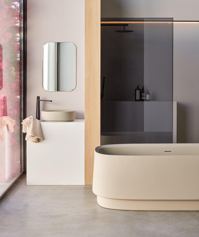 Modern bathroom with freestanding bathtub, minimalist sink with mirror, and a glass-enclosed shower. Soft lighting and neutral tones create a clean, contemporary look