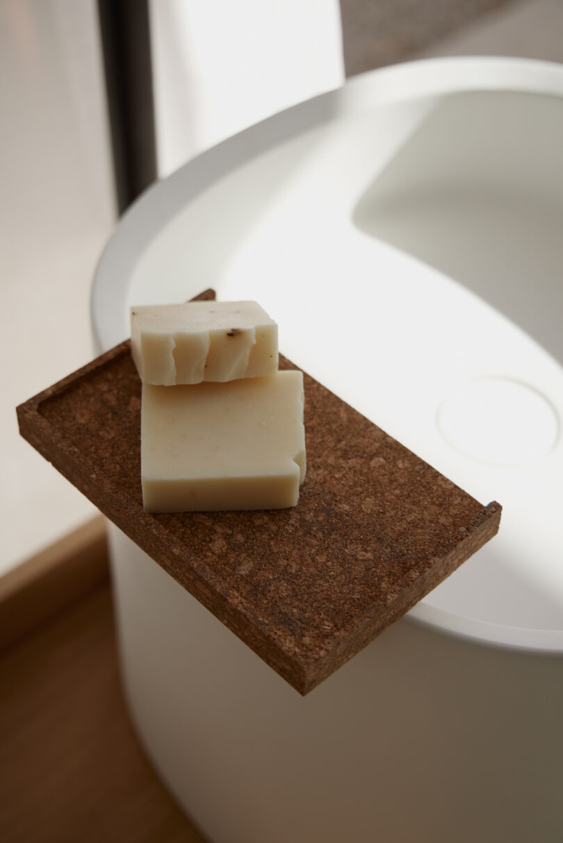 Two bars of soap on a rectangular wooden tray next to a white round sink