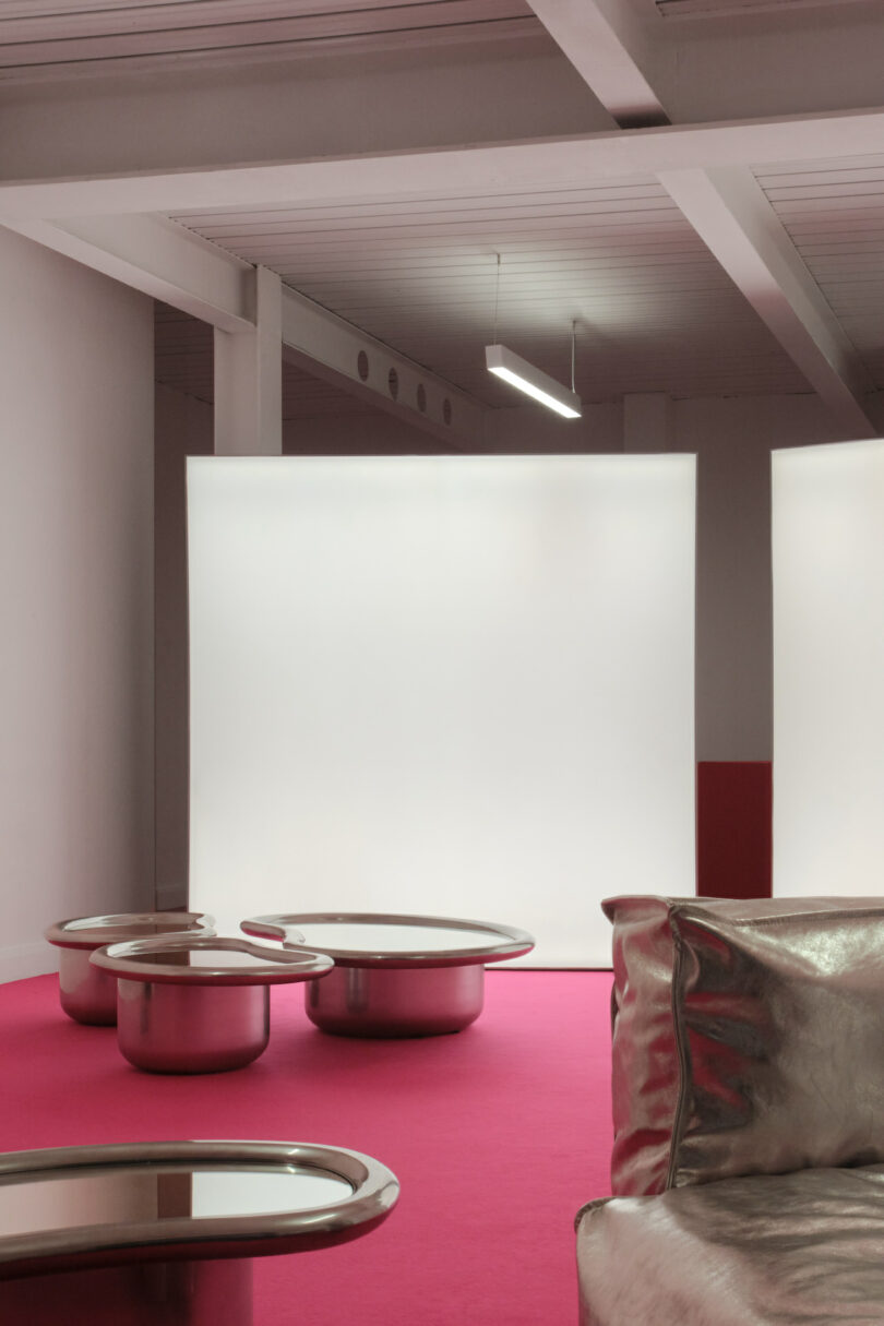 Modern room with a pink floor, metallic furniture, and a large, bright white screen in the background