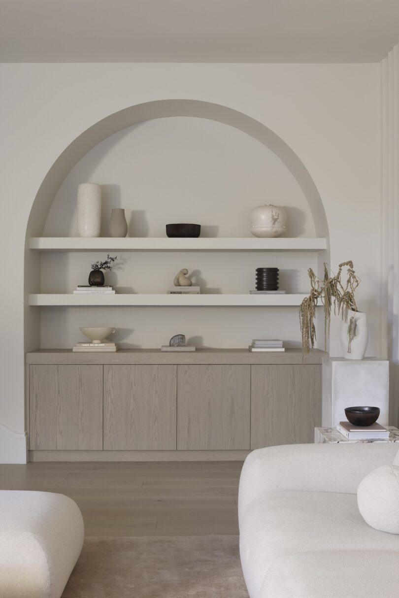 Modern living room with an arched niche, minimalist shelves with decor, and neutral-toned furniture.