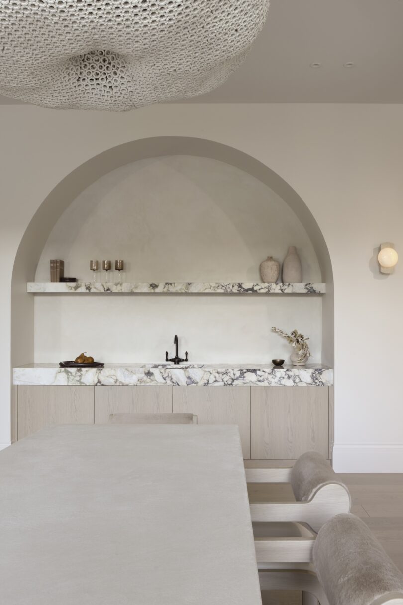 Modern minimalist kitchen with marble countertops, arched alcove, open shelving, and soft lighting. Neutral tones and contemporary decor create an elegant atmosphere.