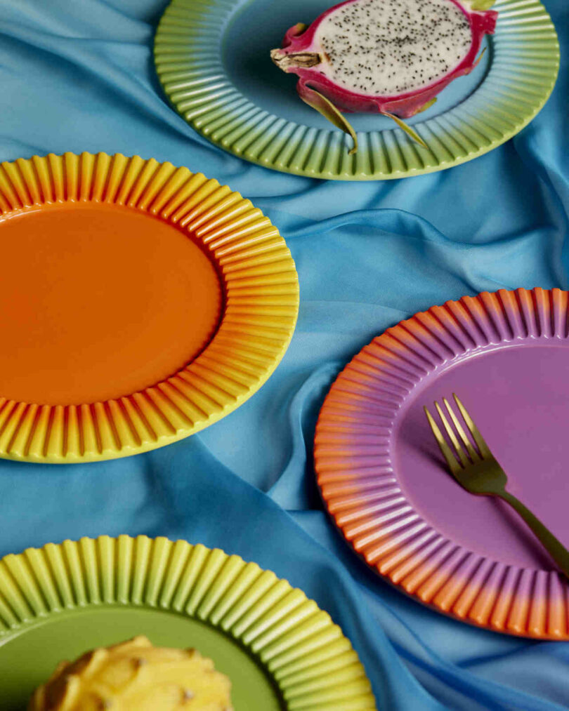 Colorful plates with a fork on a blue fabric background, featuring a sliced dragon fruit and a yellow fruit