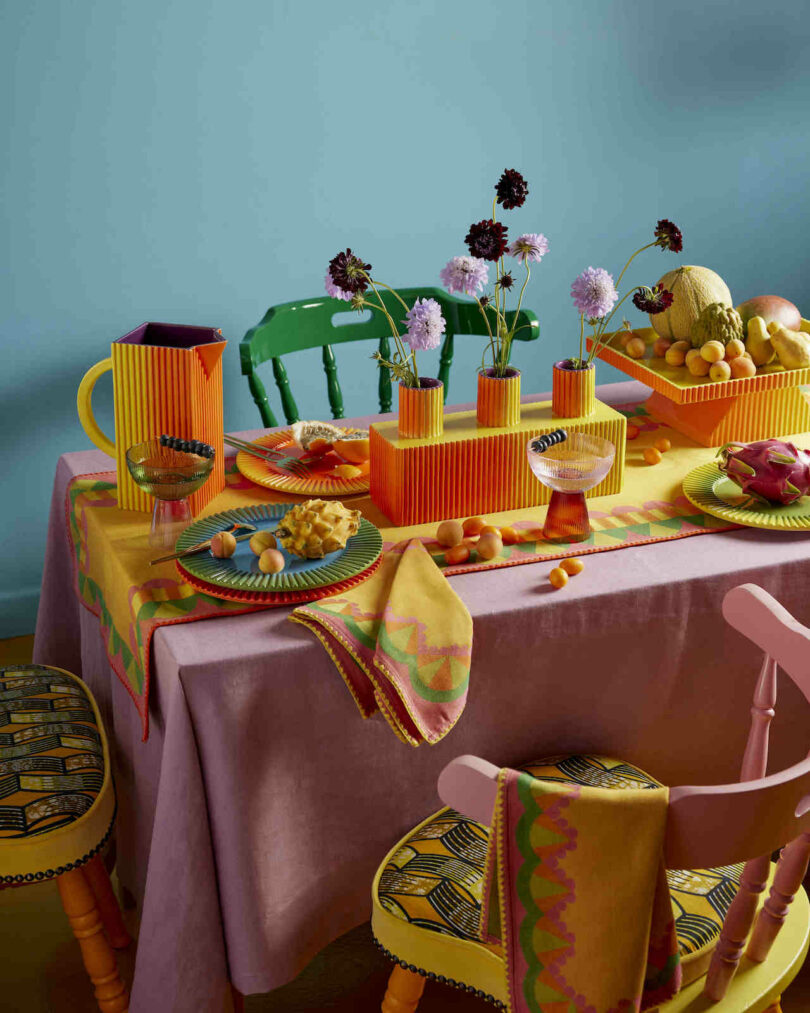 Colorful table setting with fruit, flowers in vases, and vibrant dishes on a pink tablecloth