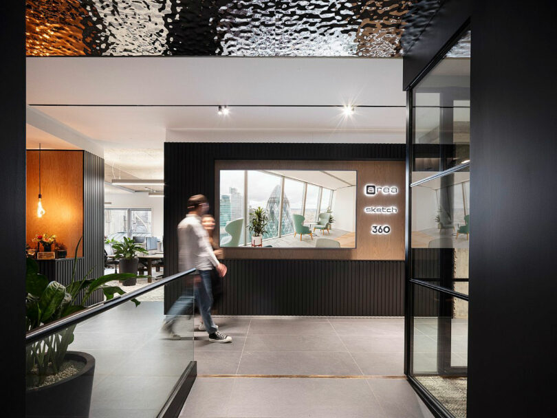 Person walking in a modern office lobby with a digital display featuring an interior design image and logos.