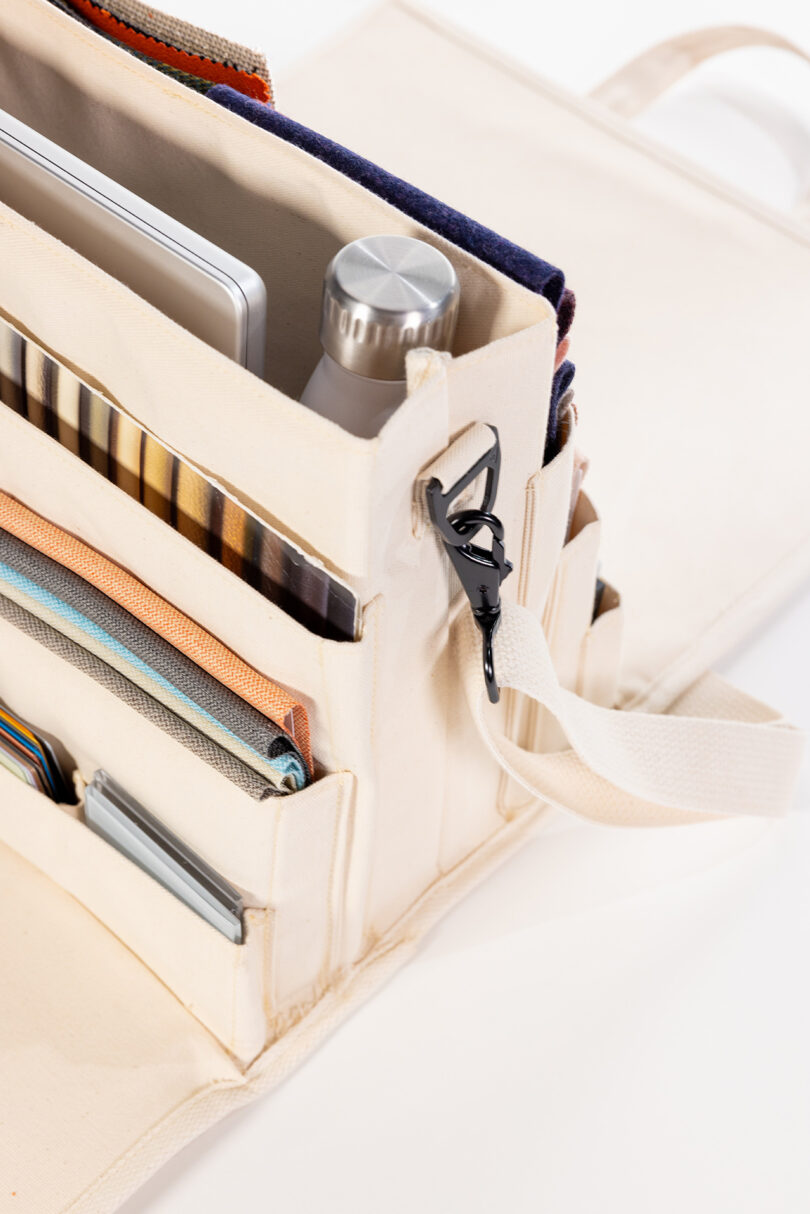 An organized bag with multiple compartments holding a water bottle, a notebook, colorful fabrics, and a phone.