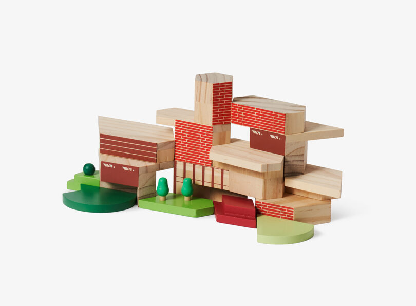 Wooden building block set arranged to resemble a modern house with red brick pattern blocks and green landscape features.