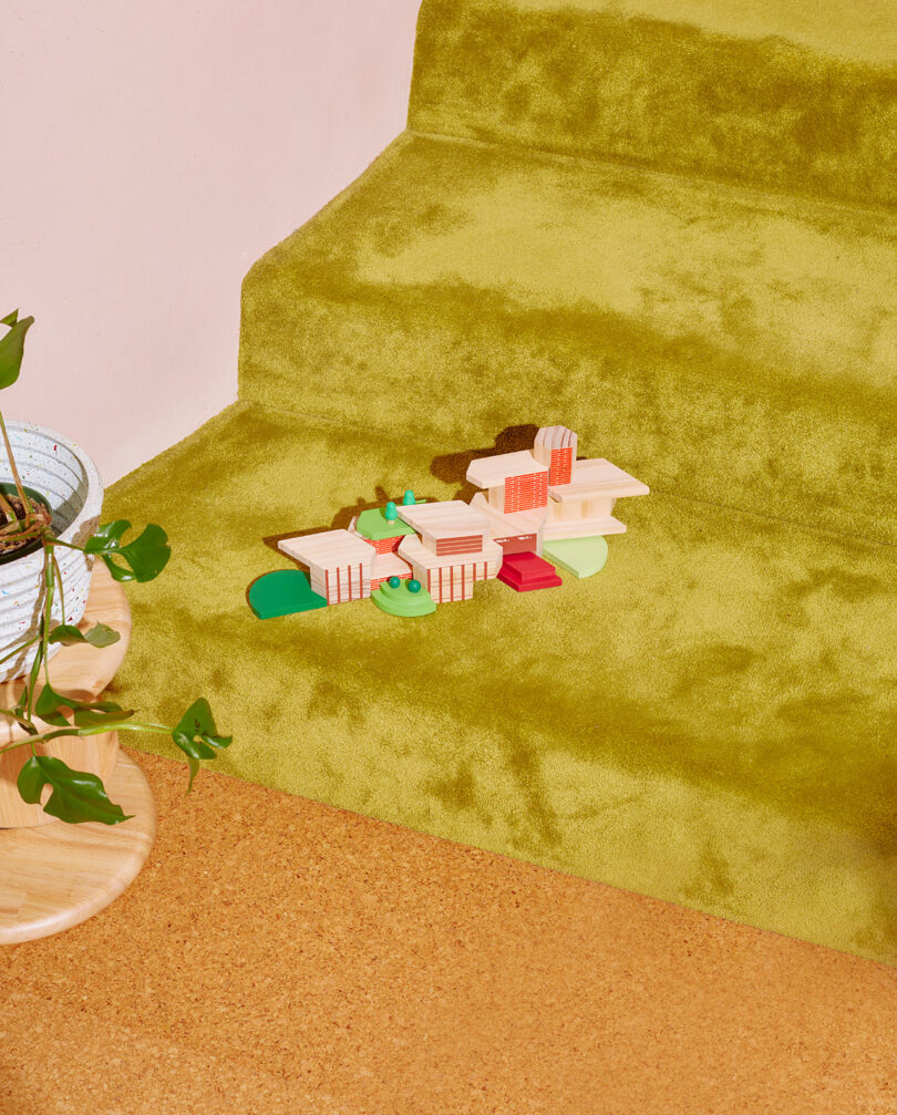 Wooden building blocks on green carpeted stairs next to a potted plant.