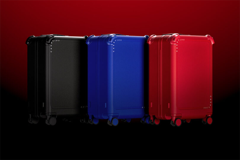 Three suitcases in black, blue, and red are standing upright against a gradient red to black background.