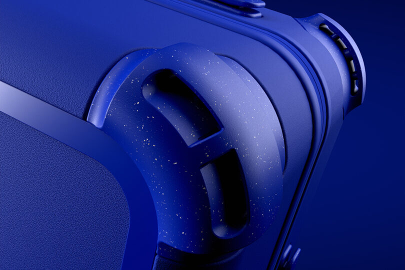 Close-up of a blue suitcase corner with a textured surface and speckled handle against a solid blue background.