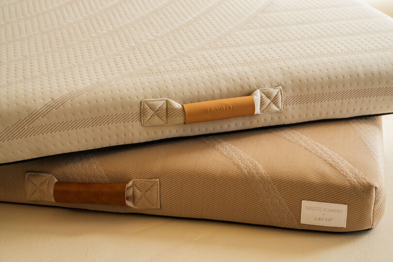 Two neatly stacked mattresses with textured, beige covers, featuring leather handles and branded tags.