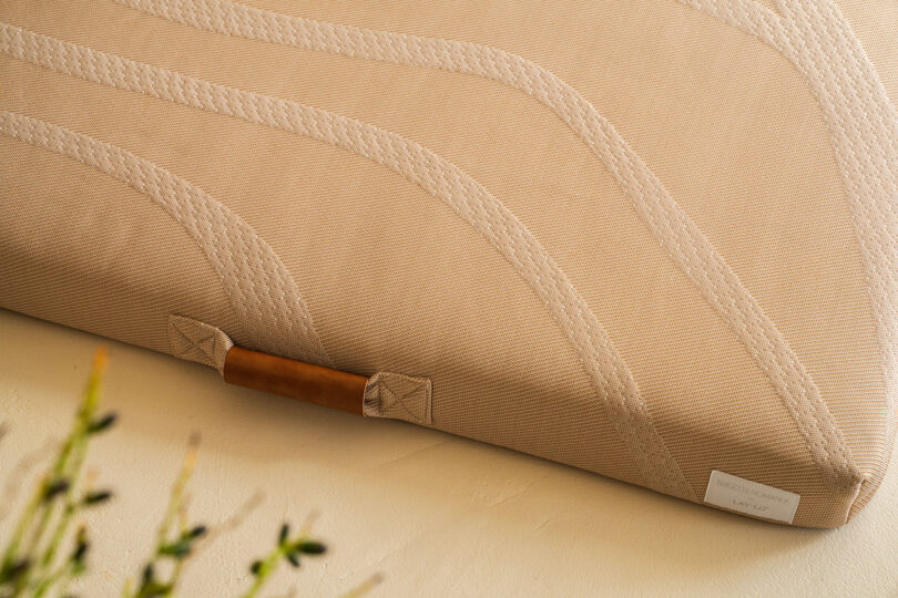 Close-up of a beige mattress with stitched wave patterns and a brown handle on a soft focus background.