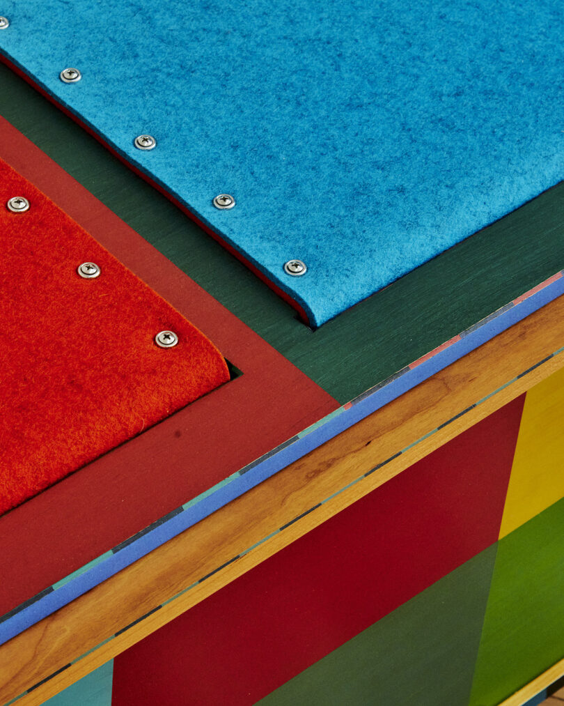 Close-up of overlapping colored panels in red, blue, and green with visible screw details and wood edges.