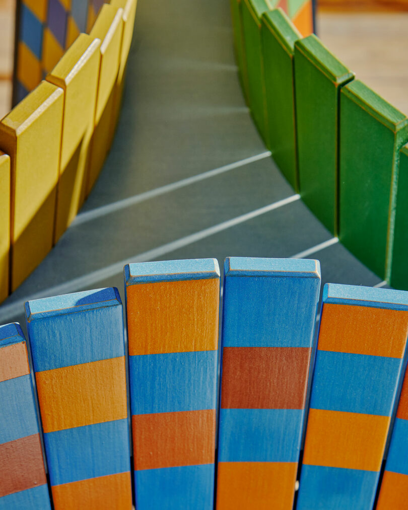 Colorama at Superhouse presents vibrant wooden blocks arranged in a captivating curve, showcasing stripes of blue, orange, yellow, and green.