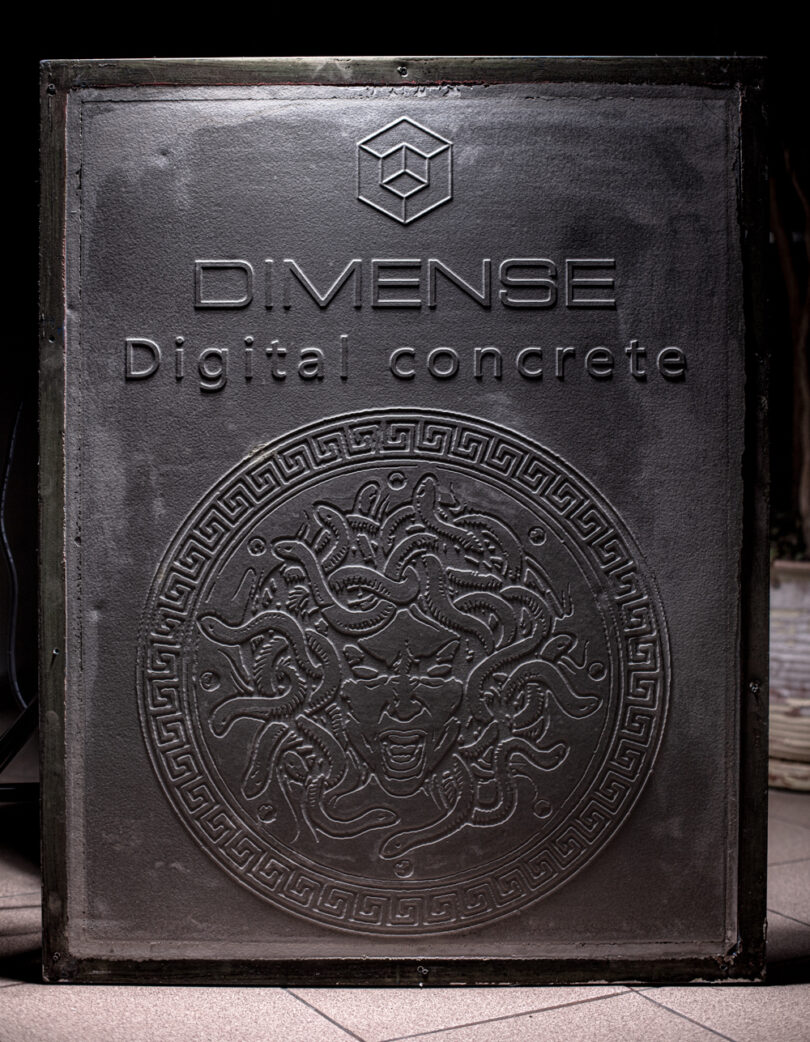 A textured panel with "DIMENSE Digital Concrete" embossed above a Medusa head design in the center