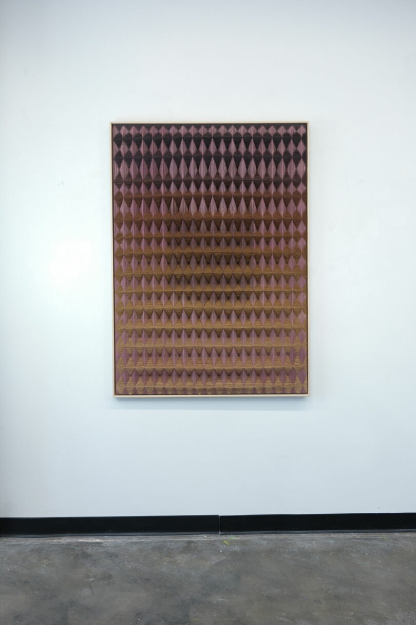 Anya Molyviatis's wall-mounted artwork showcases a grid of pink and brown 3D pyramid shapes, intricately arranged in a diamond pattern.