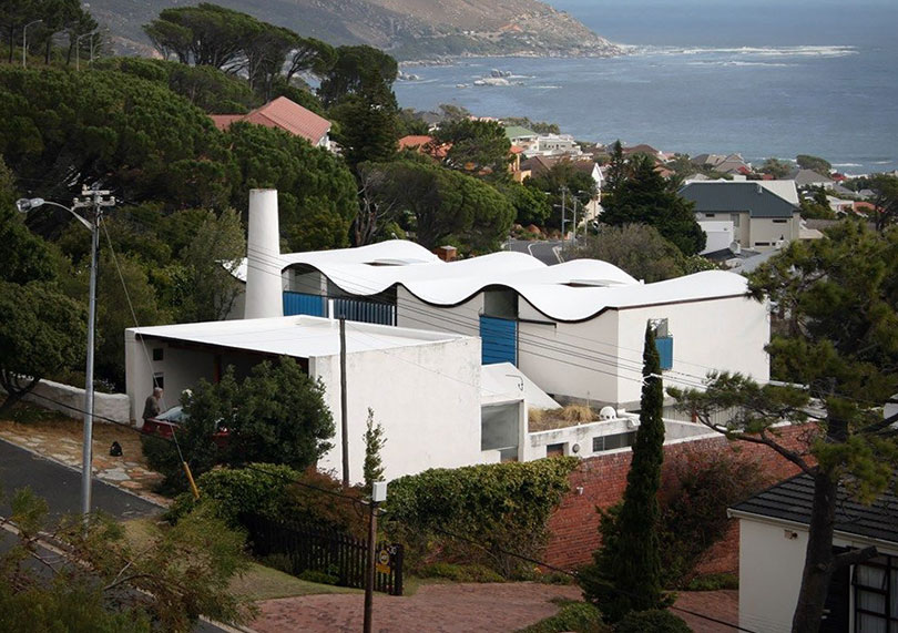 Perched on a hillside, Kevin Frankental's modern white house boasts a wavy roof and offers breathtaking views of the ocean and lush greenery.