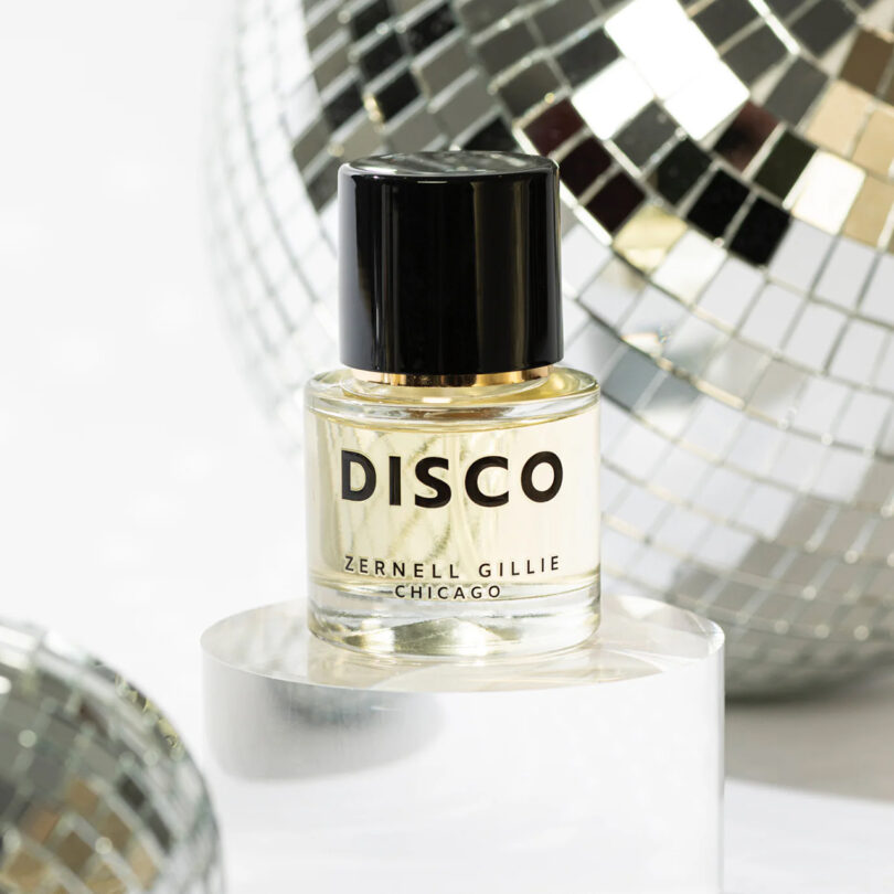 A perfume bottle labeled "DISCO" by Zernell Gillie Chicago is placed on a mirrored surface, surrounded by reflective disco balls.