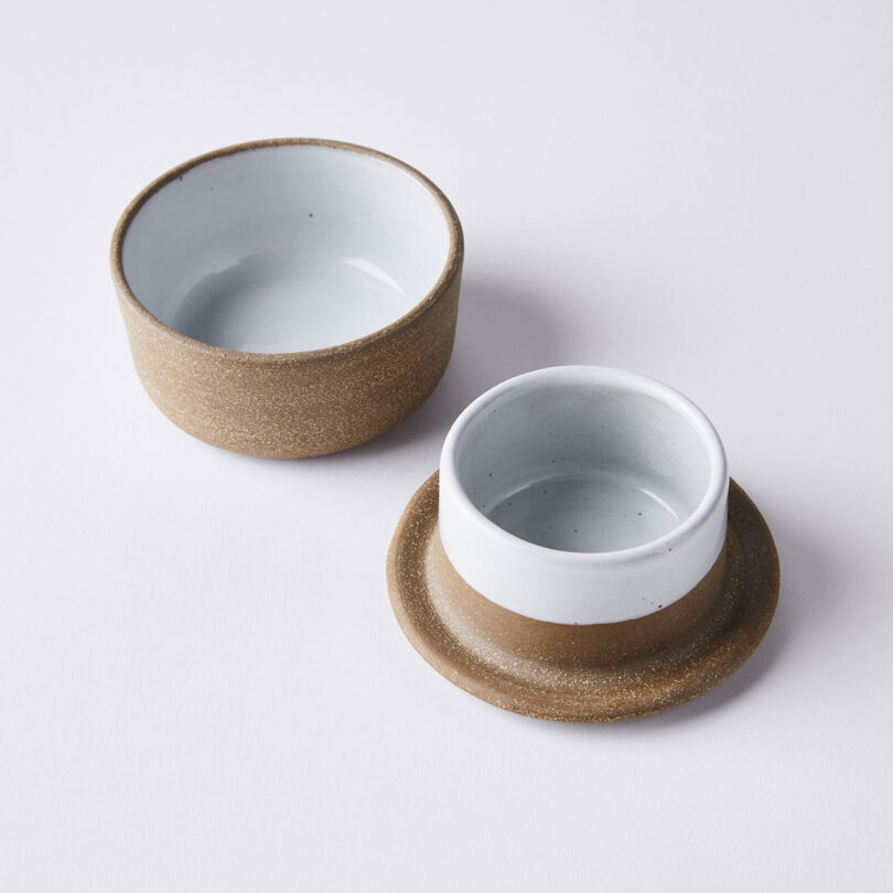 Two parts of a ceramic butter keeper sit on a white surface; one is upright, and the other is placed on a matching base.