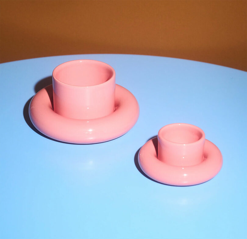 Two pink cylindrical vases with donut-shaped bases on a blue surface against a brown background.