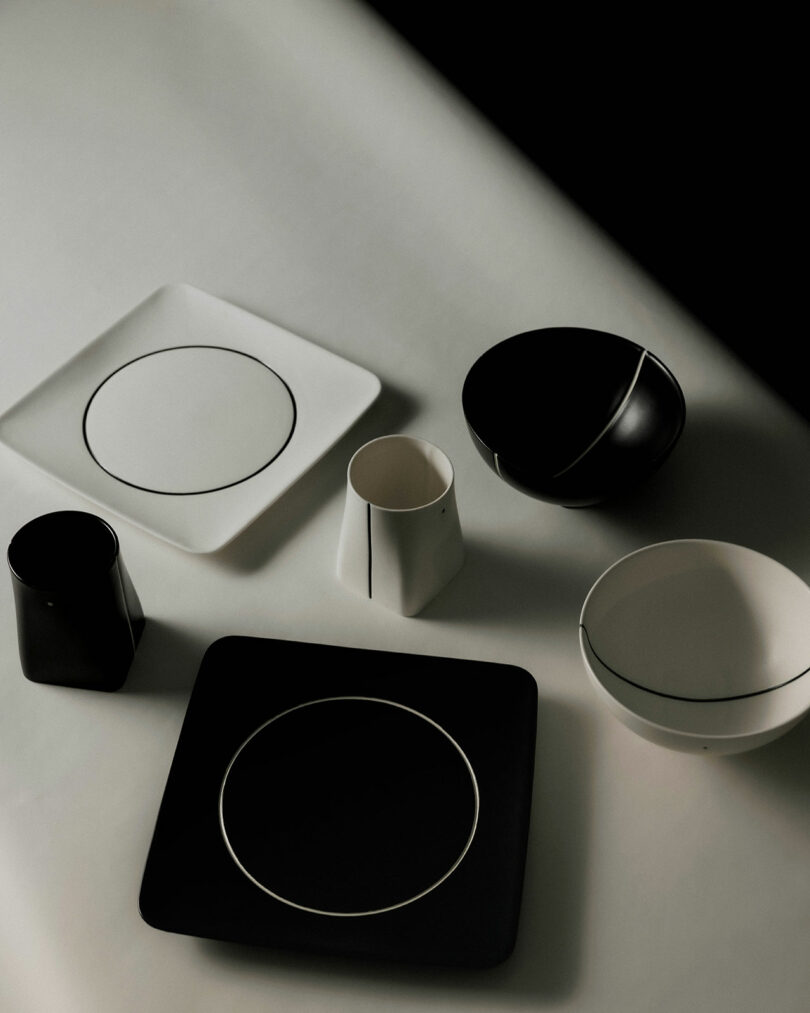 A collection of black and white geometric dishes and bowls set on a light surface, casting soft shadows.