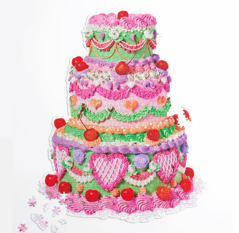 A colorful, three-tiered cake puzzle with strawberries, cherries, and heart patterns, partially assembled with scattered pieces around it.