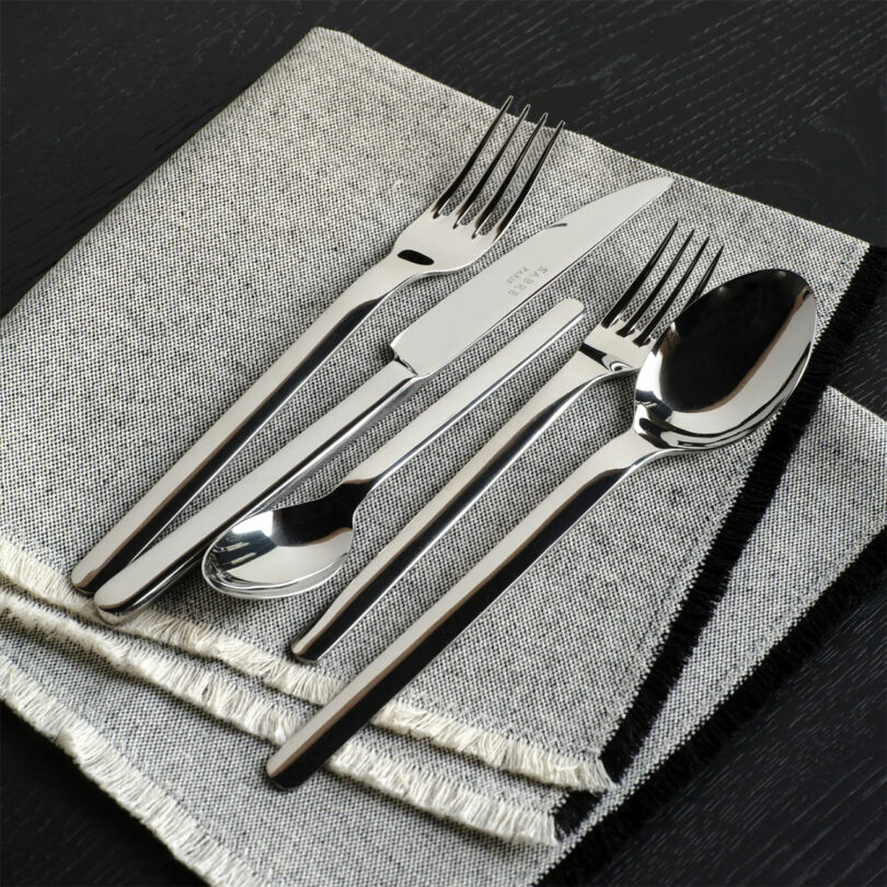 A set of silverware, including a knife, fork, tablespoon, and teaspoon, is neatly arranged on a folded gray cloth napkin.