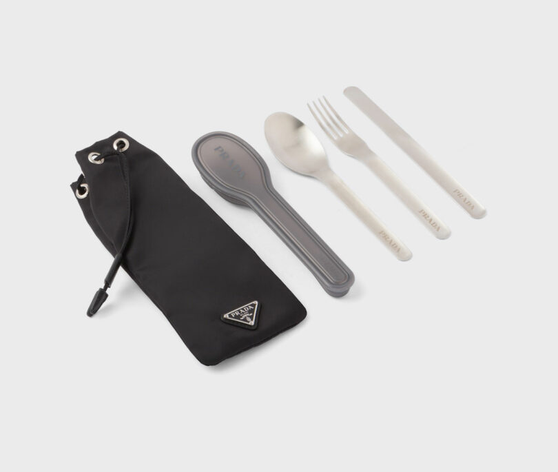 The modern gifts cutlery set includes a spoon, fork, knife, and straw neatly placed next to a sleek black carrying pouch featuring an elegant logo.